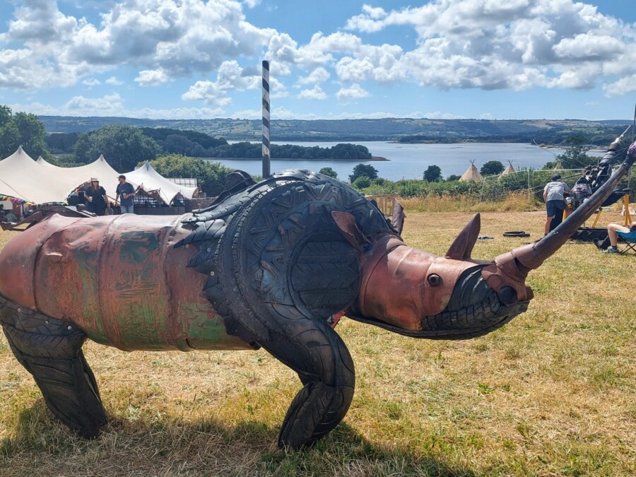 Metal sculpture of a Rhino with festival tents and a large lake in the background