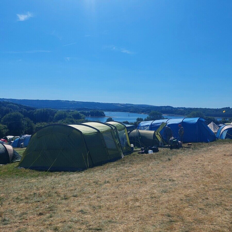 Large family tents in a field overlooking a large lake and a clear blue sky.