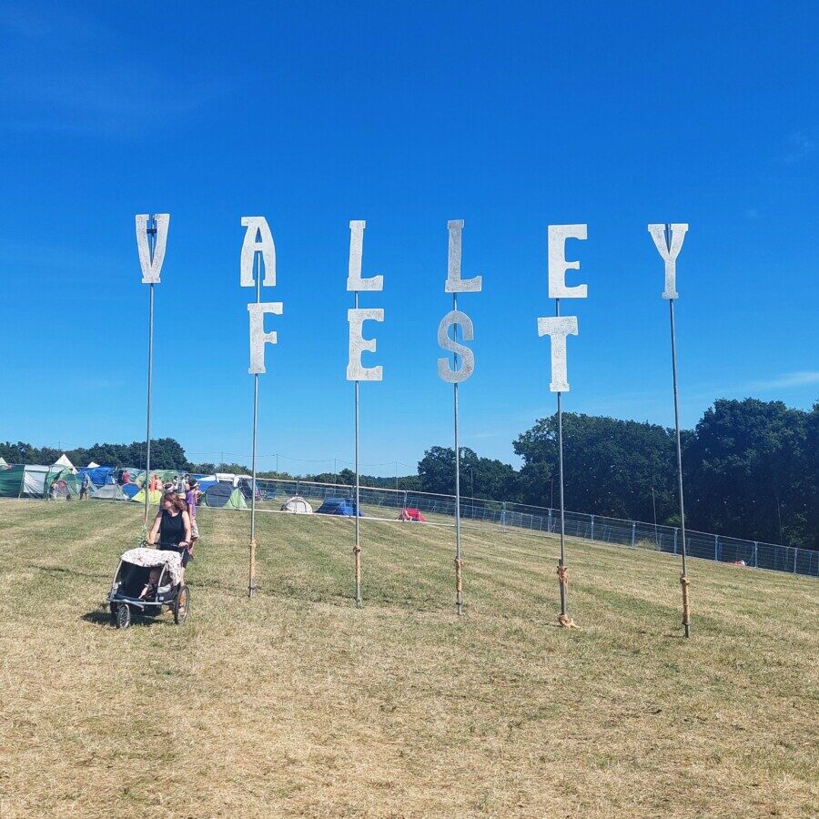 Giant silver letters on posts, spelling out the words Valley Fest. A woman with a double buggy is walking through the posts.